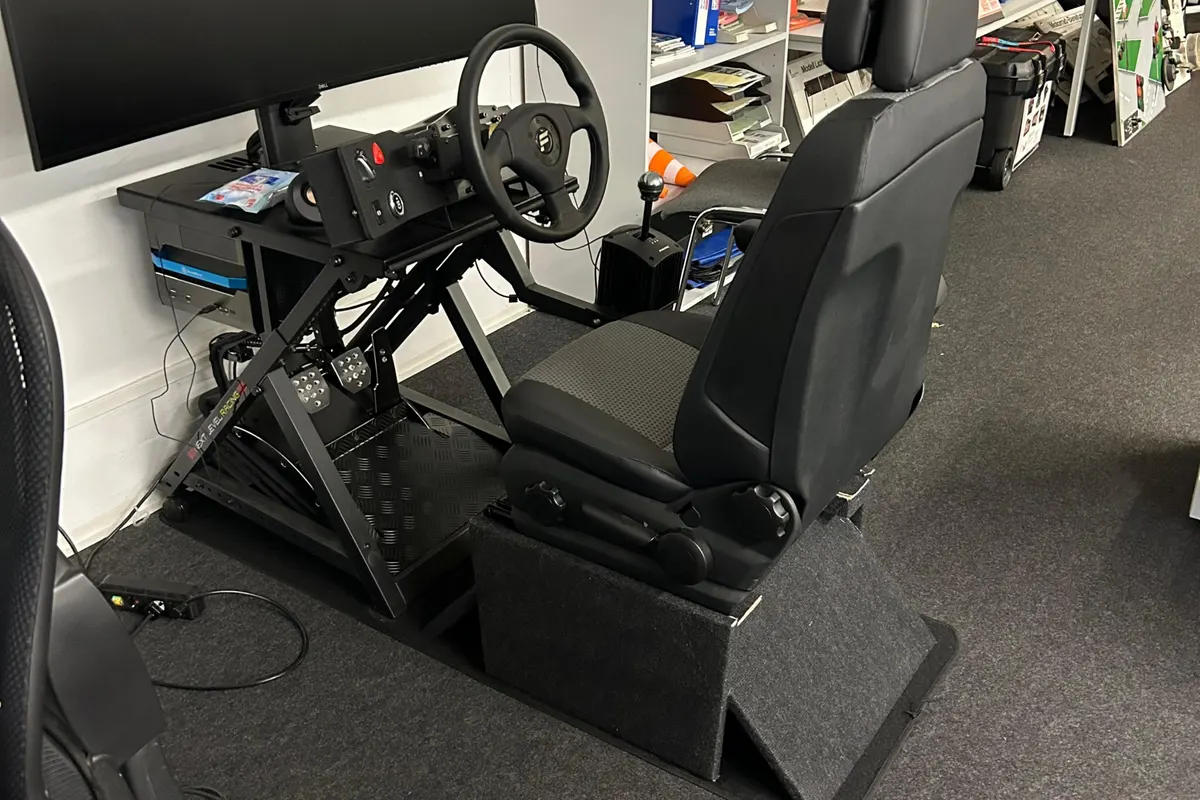 Fahrsimulator mit Sitz, Lenkrad und drei Bildschirmen in einem Schulungsraum